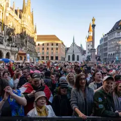 Bunte Menge feiert ausgelassen Fasching am Marienplatz in München. Menschen in Kostümen jubeln und tanzen vor historischer Kulisse.