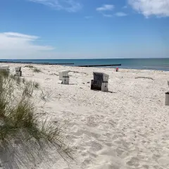 Hiddensee Strand mit Strandkörben und Dünen. Das Meer glänzt in der Sonne, ein einsamer Mensch spielt im Sand.