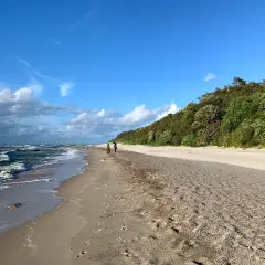 Spaziergang am Strand von Dranske Bakenberg. Wellen brechen an der Küste, während zwei Personen den Sandweg entlanggehen.