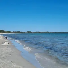 Sonniger Tag am Juliusruh Strand. Menschen entspannen sich am Sand, Kinder bauen Sandburgen, andere baden im ruhigen Meer.