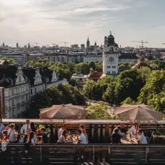 Menschen genießen das Leben auf einem **rooftop Munich** mit Blick auf die Stadt und den Turm.