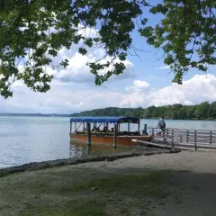 Ein Ausflugsboot wartet am Steg am Starnberger See. Zwei Männer sitzen auf einer Bank im Schatten.