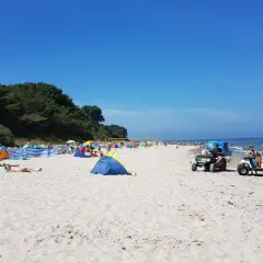 Sonniger Strandtag in Nonnewitz an der Ostsee. Menschen entspannen unter bunten Zelten, während Strandverkäufer Eis und Getränke anbieten.