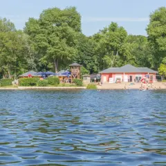 Sommerfreude an einem der **besten Badeseen Berlins**: Menschen planschen im Wasser, entspannen am Sandstrand und genießen die Sonne.