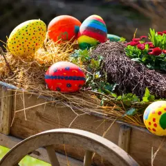 Bunte Ostereier und Blumen schmücken einen alten Wagen, perfekt für Ostermontag Veranstaltungen.
