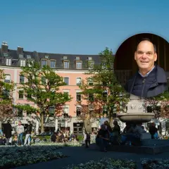 Ein Mann lächelt vor einem Brunnen und rosa Gebäuden im Glockenbachviertel München.