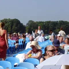 Menschen auf einem Schiff genießen eine Muttertag Unternehmung. Sie sitzen auf blauen Stühlen und blicken auf das Wasser.