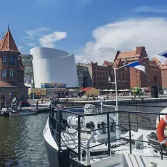Hafenansicht mit historischer Backsteinarchitektur und modernem Gebäude. Ein Schiff mit Rettungsring liegt im Vordergrund. Stralsund sehenswertes Panorama.
