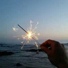 Ein Wunderkerze leuchtet am Silvesterabend am Strand. Die Funken tanzen über dem ruhigen Meer und dem klaren Himmel.