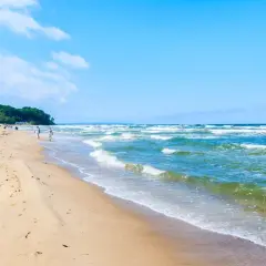 Ein sonniger Tag am Ostseebad Baabe. Menschen spazieren am breiten Sandstrand entlang, während die Wellen der Ostsee sanft ans Ufer rollen.