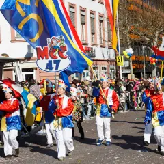 Bunte Kostüme und Fahnen beim Fasching 2026. Menschen feiern ausgelassen in der Stadt.
