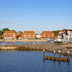Hafen mit roten Ziegeldächern, Booten und einem Kirchturm im Hintergrund.