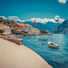 Blick auf eine malerische Küstenstadt mit roten Dächern und einem Kirchturm, umgeben von Bergen. Boote schaukeln auf dem türkisfarbenen Wasser. Ein Traumziel!