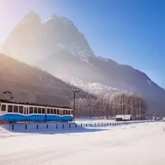 Blauer Zug fährt durch verschneite Alpenlandschaft, tolle Winterurlaub Ideen für Ihre Reise.