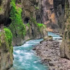 Türkisblaues Wasser rauscht durch die enge Klamm in Bayern. Ein schmaler Weg führt entlang der moosbewachsenen Felswände.