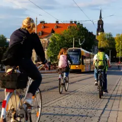 Fahrradfahrer mit Rucksäcken genießen das Bikepacking Deutschland. Eine Straßenbahn fährt vorbei, während Menschen auf Kopfsteinpflaster radeln und gehen.