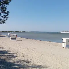 Sonniger Schaprode Strand mit Strandkörben und einem Ausflugsschiff auf dem ruhigen Meer.