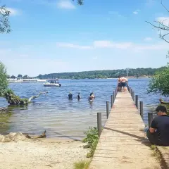 Sommer am ummanz strand: Menschen planschen im Wasser, andere sitzen am Steg. Ein sonniger Tag am See.