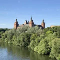 Schloss Johannisberg, ein malerisches Ziel im Spessart, ragt über üppige Bäume am Flussufer auf.