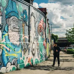 Mann geht an bunter Street Art in München vorbei. Die Wand ist mit fantasievollen Figuren und Mustern bemalt.