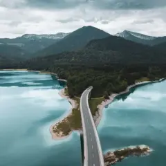 Brücke über türkisfarbenen See, umgeben von bewaldeten Bergen. Ein malerischer Ort für besondere Ausflugsziele.