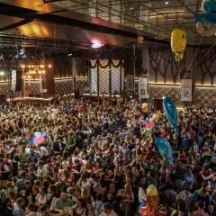 Volles Festzelt beim Starkbierfest Nockherberg. Menschen in Tracht feiern ausgelassen, mit Bierkrügen in den Händen und bunten Ballons über ihnen.