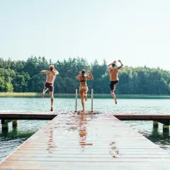 Drei Freunde springen von einem Steg in den See der Mecklenburgischen Seenplatte. Ein perfekter Sommertag am mecklenburgische seenplatte strand.