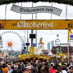 Volle Gassen beim Oktoberfest. Ein Schild verkündet "Willkommen zum Oktoberfest". Eintritt kostet das Oktoberfest nicht, aber die Attraktionen und das Bier.