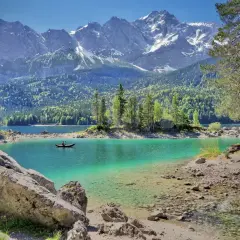 Türkiser Bergsee in Deutschland mit schneebedeckten Gipfeln im Hintergrund. Ein Kanufahrer genießt die Ruhe.