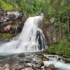 Tosender Wasserfall im Teutoburger Wald, umgeben von Felsen und üppigem Grün. Das Wasser stürzt tosend in ein türkisfarbenes Becken.