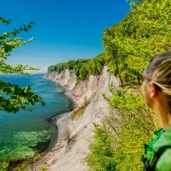 Frau blickt auf Kreidefelsen im Nationalpark Jasmund. Türkisfarbenes Meer und grüne Bäume.