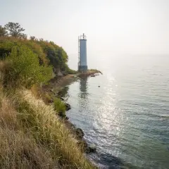 Leuchtturm auf der Halbinsel Zudar, umgeben von üppiger Vegetation und dem glitzernden Meer.