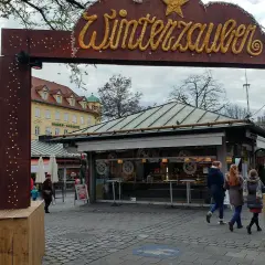 Der Viktualienmarkt zeigt seinen Winterzauber. Menschen schlendern vorbei an Ständen, die auf den Weihnachtsmarkt einstimmen.