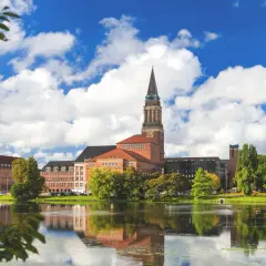 Ein malerischer Blick auf das Rathaus von Kiel, perfekt für Kiel Sightseeing. Der Turm ragt in den blauen Himmel, während sich das Gebäude im ruhigen Wasser spiegelt.