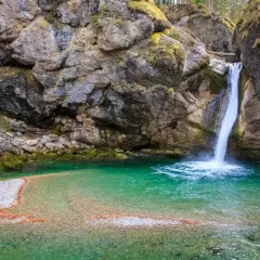 Türkiser bergsee mit einem tosenden wasserfall, der in die klare Tiefe stürzt. Felsen und Moos umrahmen dieses Naturschauspiel.
