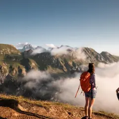 Zwei Frauen mit Rucksäcken genießen den Ausblick nach einem erfolgreichen Rosskopf Wandern. Wolken ziehen durch die Berge.