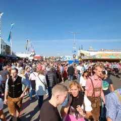 Menschenmassen auf dem Oktoberfest 2026, viele in Tracht, unter blauem Himmel.