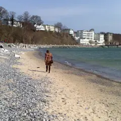Eine Frau spaziert am Strand entlang, im Hintergrund die Bäderarchitektur von Sassnitz.