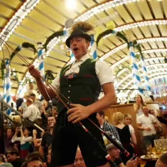 Mann im bierzelt oktoberfest mit Peitsche, jubelnde Menge im Hintergrund.