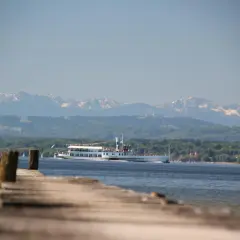 Holzsteg am Ammersee mit einem Ausflugsschiff, im Hintergrund die schneebedeckten Ammersee Berge.