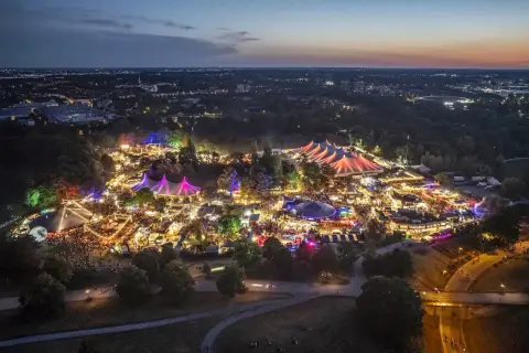 Nachtansicht des beleuchteten Tollwood Festivals im Olympiapark München mit bunten Zelten und Lichtern.