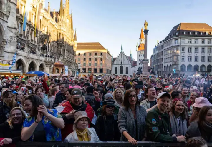 Bunte Menge feiert ausgelassen Fasching am Marienplatz in München. Menschen in Kostümen jubeln und tanzen vor historischer Kulisse.