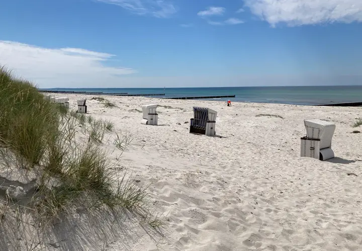 Hiddensee Strand mit Strandkörben und Dünen. Das Meer glänzt in der Sonne, ein einsamer Mensch spielt im Sand.