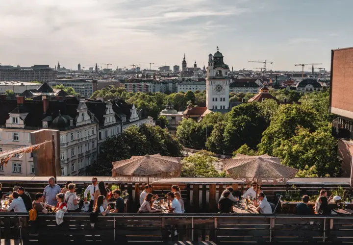 Menschen genießen das Leben auf einem **rooftop Munich** mit Blick auf die Stadt und den Turm.