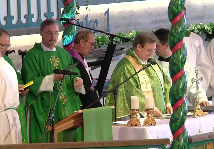 Priester in grünen Gewändern bei einem Gottesdienst in den Kirchen. Kerzen und ein Kreuz stehen auf dem Altar.