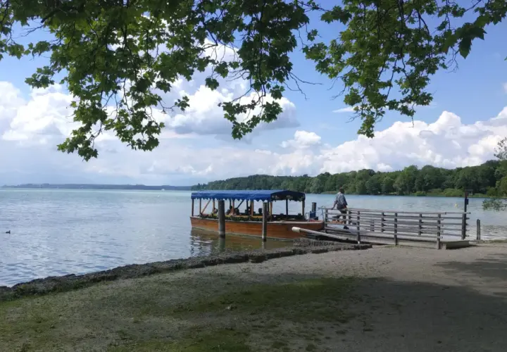 Ein Ausflugsboot wartet am Steg am Starnberger See. Zwei Männer sitzen auf einer Bank im Schatten.