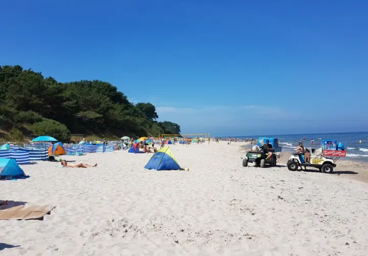Sonniger Strandtag in Nonnewitz an der Ostsee. Menschen entspannen unter bunten Zelten, während Strandverkäufer Eis und Getränke anbieten.