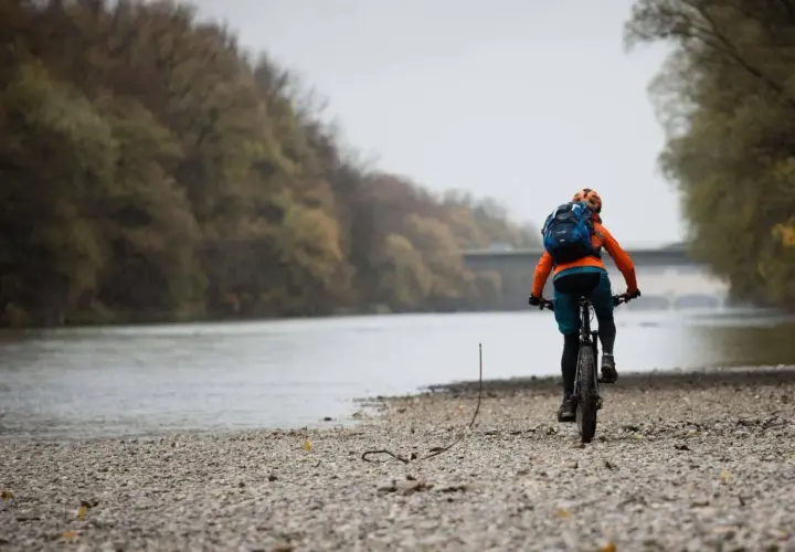 Radfahrer auf den Isar Trails, mit Rucksack und Helm, fährt am Flussufer entlang.