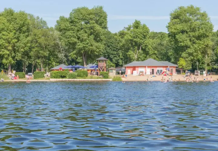 Sommerfreude an einem der **besten Badeseen Berlins**: Menschen planschen im Wasser, entspannen am Sandstrand und genießen die Sonne.