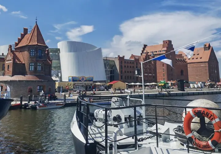 Hafenansicht mit historischer Backsteinarchitektur und modernem Gebäude. Ein Schiff mit Rettungsring liegt im Vordergrund. Stralsund sehenswertes Panorama.